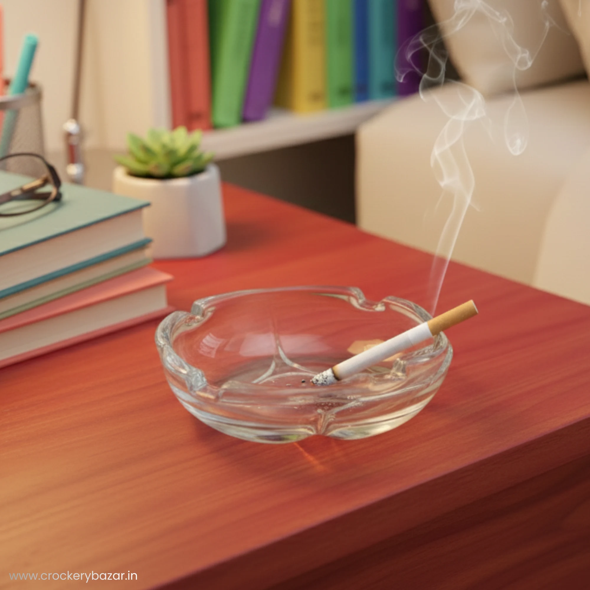 A clear glass ashtray on a wooden bedside table next to a stack of books and a small plant.