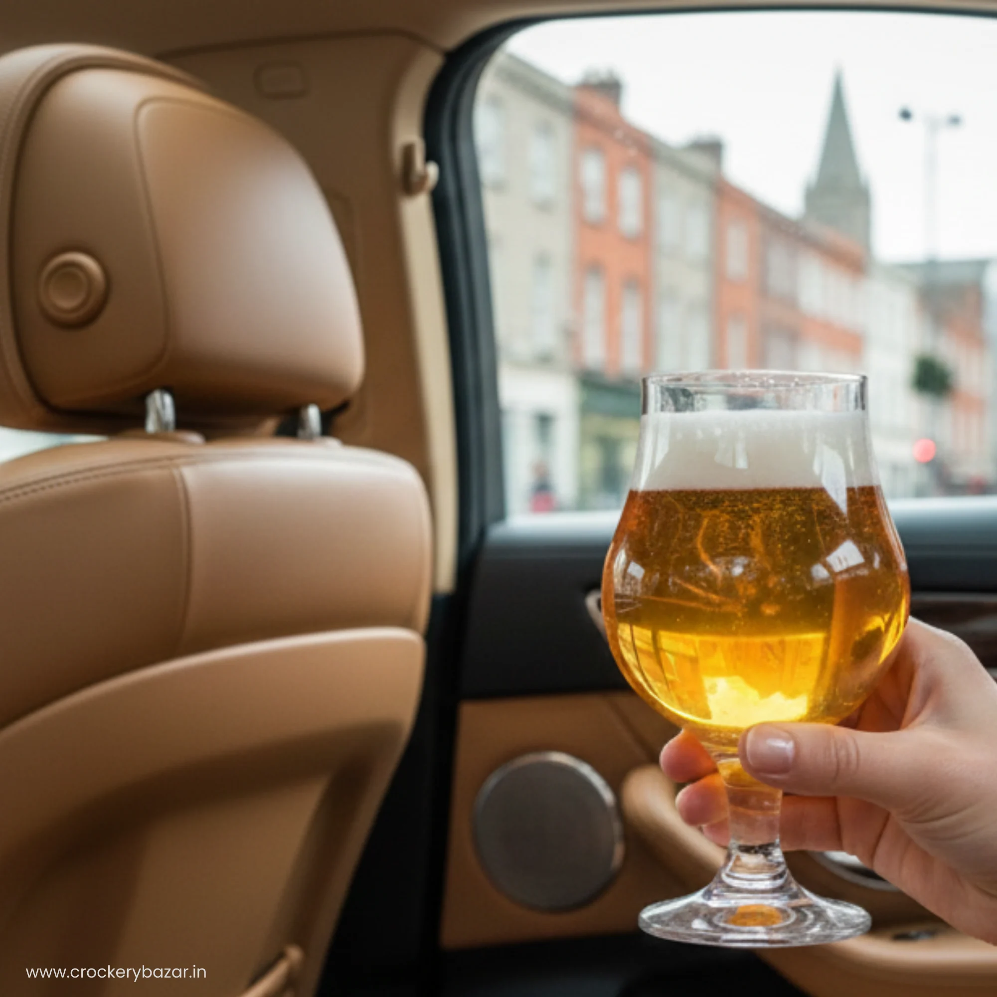 A hand holding a Dublin 400 ml stemmed beer glass filled with golden lager inside a luxury car with a city view.