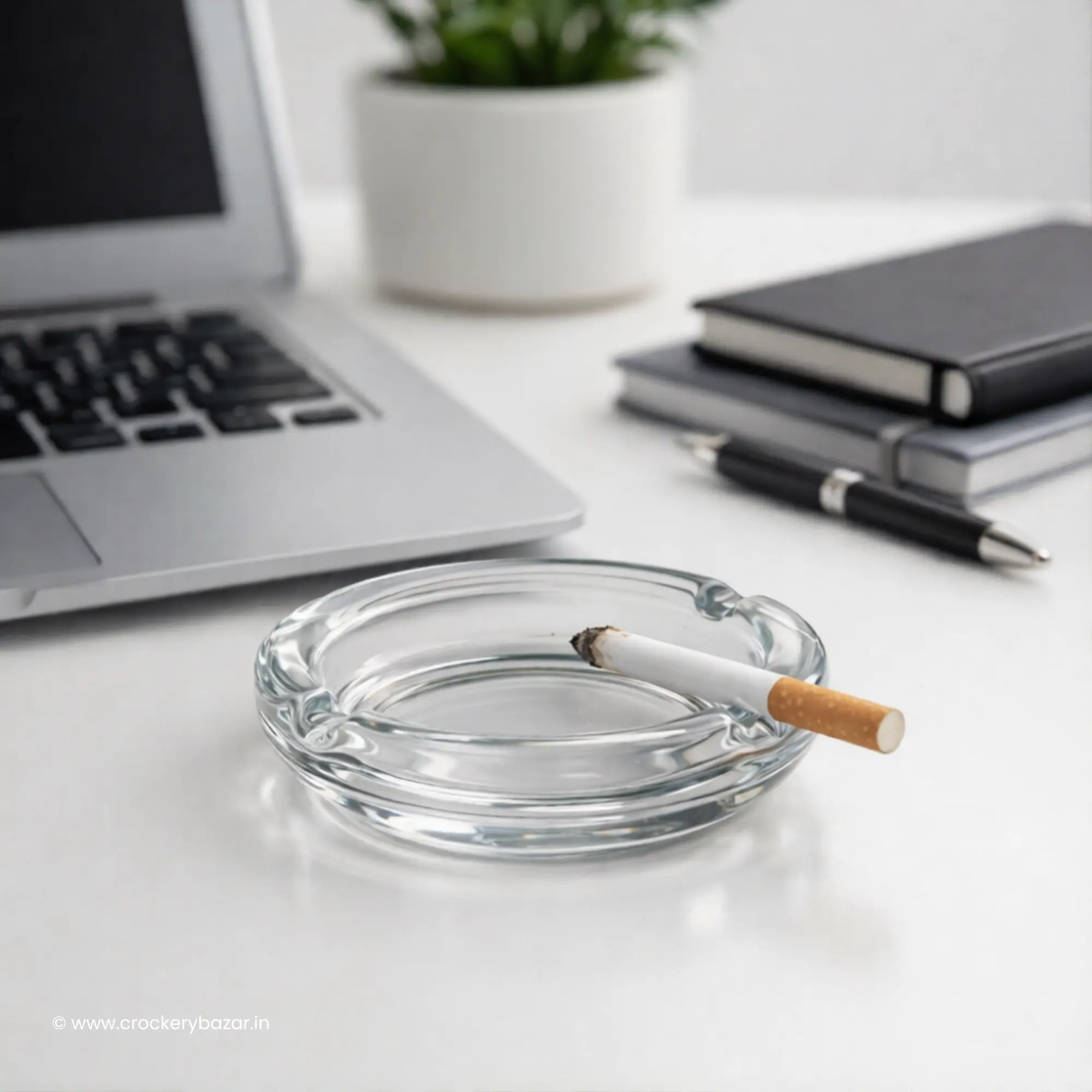 Bormioli Rocco Poker glass ashtray positioned on a white minimalist home office desk near a laptop.
